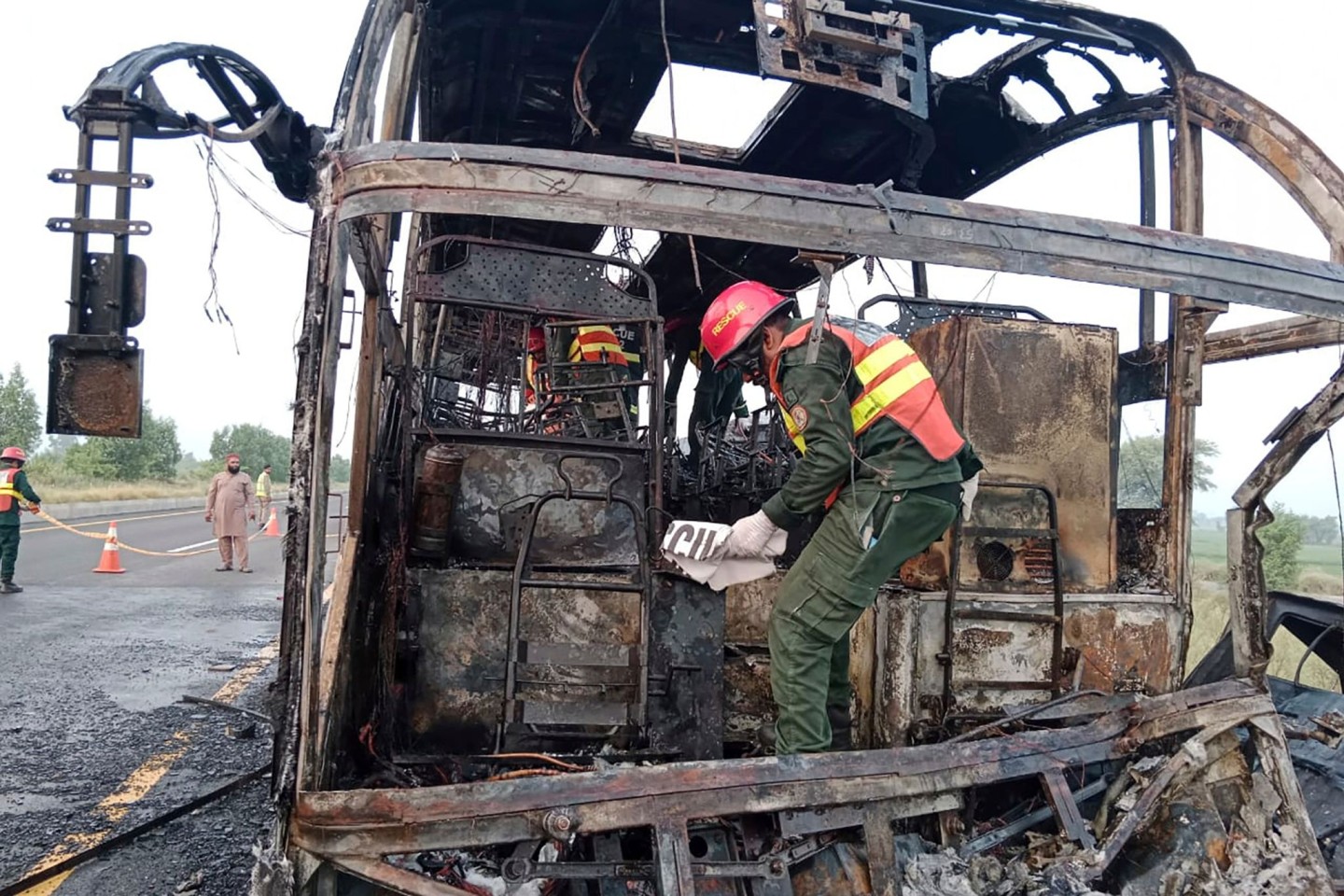 Rettungskräfte untersuchen den verbrannten Bus an der Unfallstelle auf einer Autobahn.