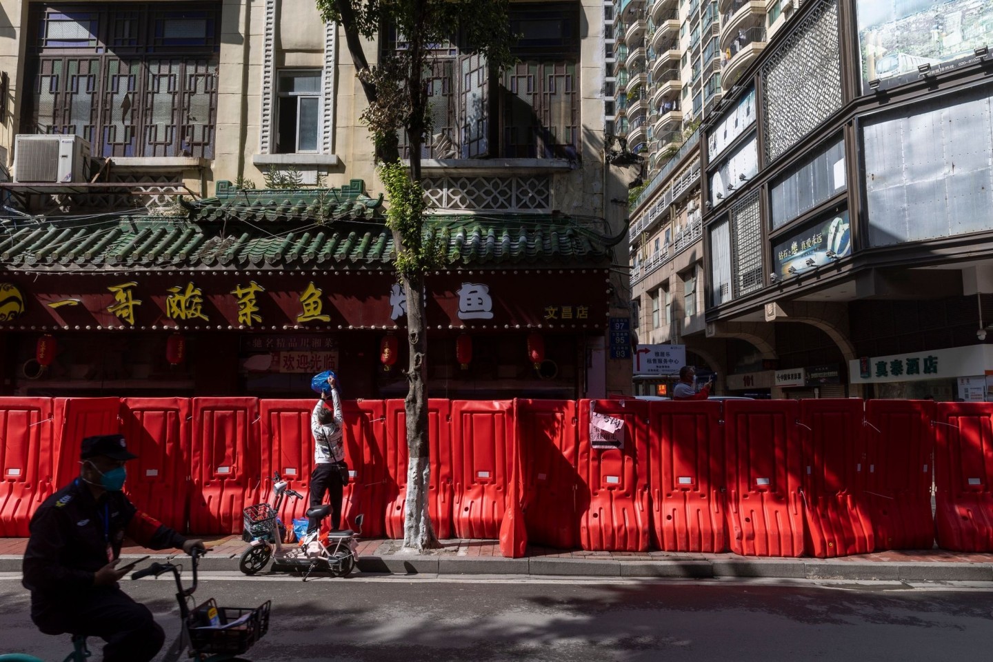 Ein Bewohner reicht Gegenstände über eine provisorische Absperrung in der Metropole Guangzhou, die errichtet wurde, um einen Wohnblock mit hohem Covid-19-Infektionsrisiko abzusperren.