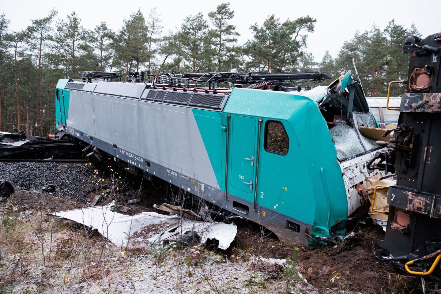 Ein entgleister Triebwagen vom aufgefahrenen Güterzug liegt beschädigt auf Schienen und Bahndamm.