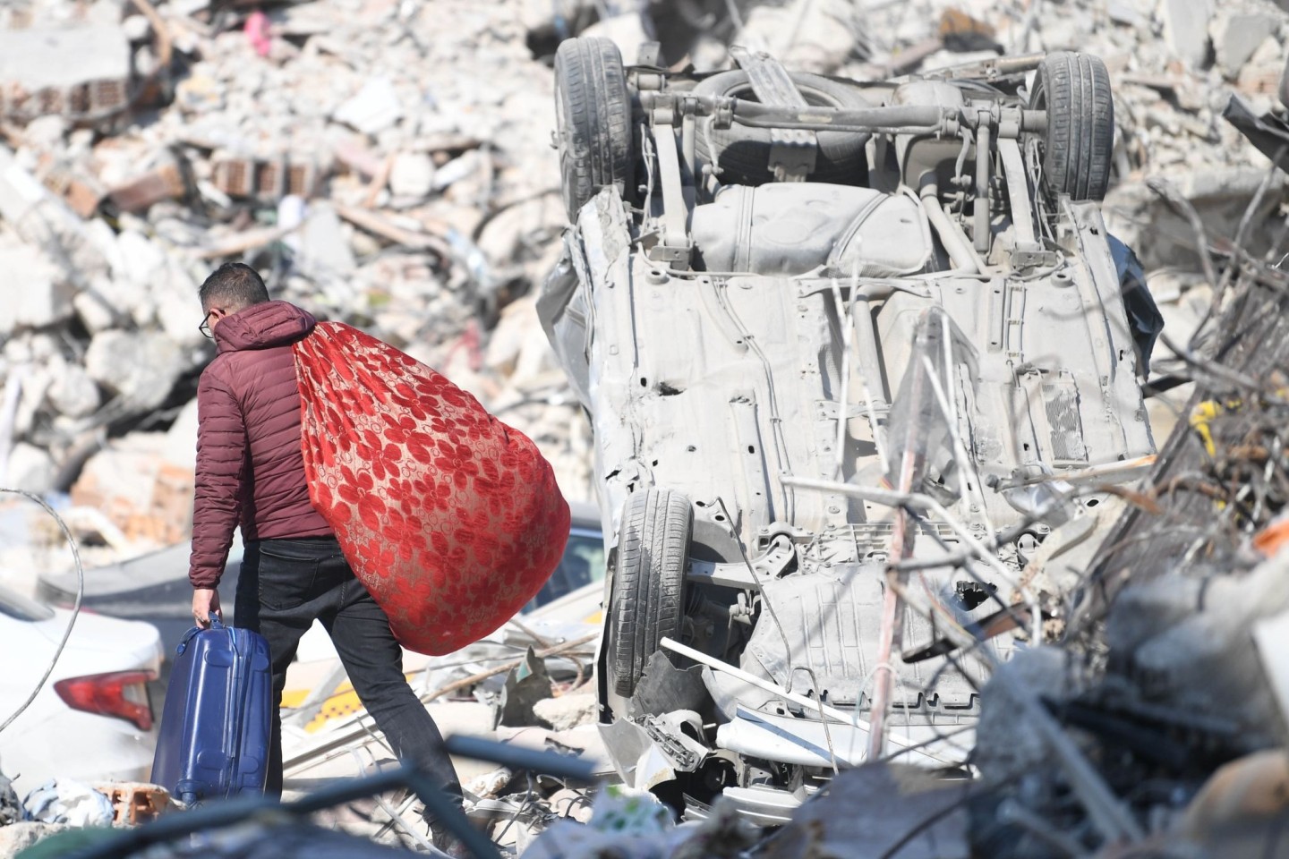 Ein Mann läuft mit seinen Habseligkeiten über Erdbebentrümmer in Antakya.