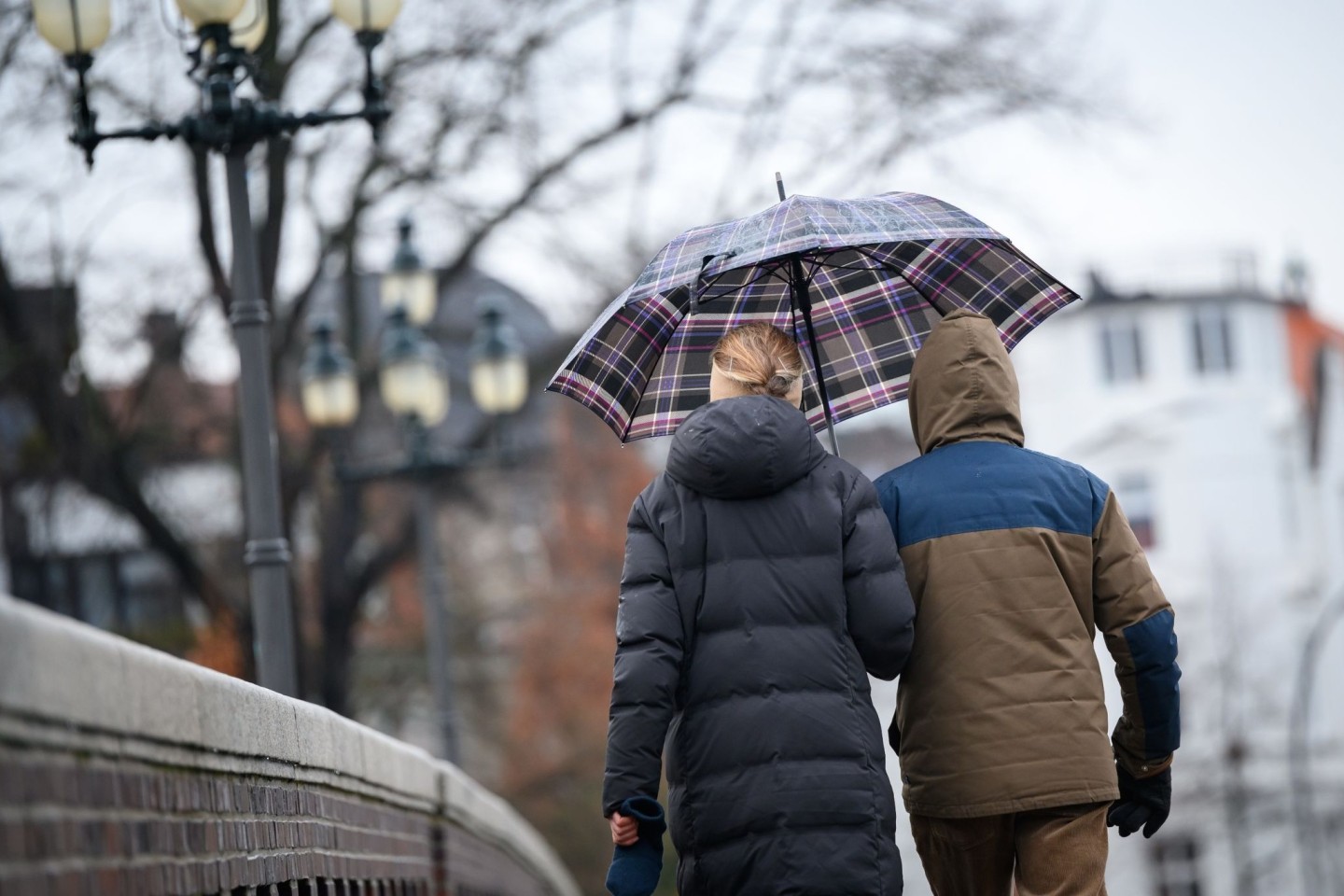 Spaziergänger laufen mit Schirm über eine Brücke in Hamburg.