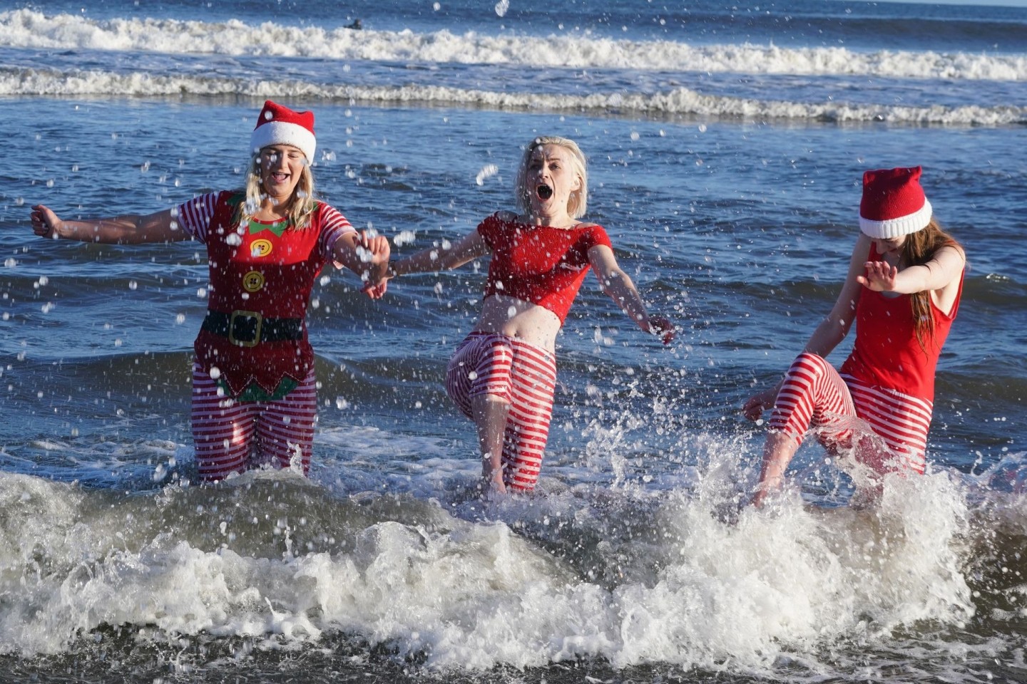 Eine Gruppe junger Frauen in Weihnachtskostümen planscht während des jährlichen Weihnachtsschwimmens am Long Sands Beach.